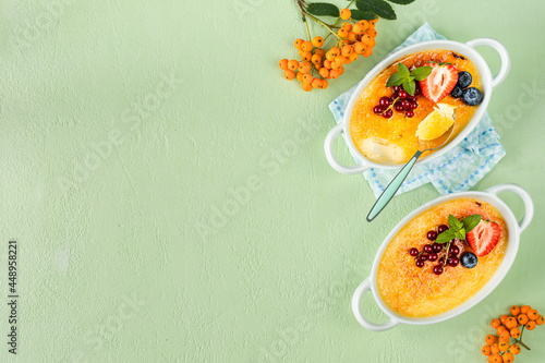 Two creme brulee desserts with fresh strawberries, currants and blueberries on a green stone table.