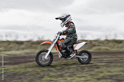 Fototapeta Naklejka Na Ścianę i Meble -  Child on his small motorcycle. Small biker dressed in a protective suit and helmet. The kid is engaged in motocross.