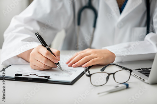 Close up of female doctor working on a laptop with writing a medical record after diagnosis, information patients, health reports, Telemedicine and Health Care Concept.