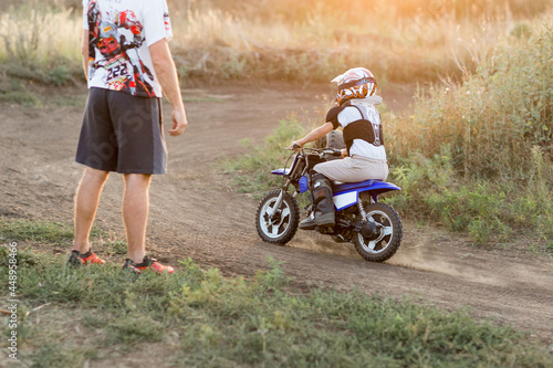 Kid on a motorcycle doing motocross. A little boy learns to ride a motorbike. The coach teaches the child to drive a motorcycle. Son and father on the track.
