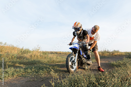 Kid on a motorcycle doing motocross. A little boy learns to ride a motorbike. The coach teaches the child to drive a motorcycle. Son and father on the track.