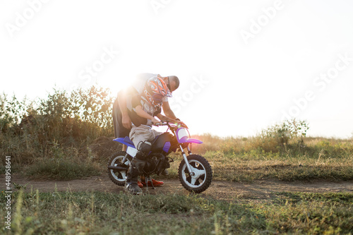 Fototapeta Naklejka Na Ścianę i Meble -  Kid on a motorcycle doing motocross. A little boy learns to ride a motorbike. The coach teaches the child to drive a motorcycle. Son and father on the track.