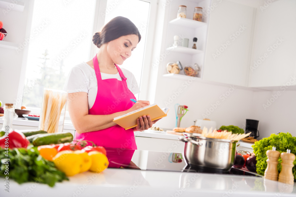Photo portrait woman in pink apron writing notes in blocknote cooking pasta Photo portrait woman in pink apron writing notes in blocknote cooking pasta