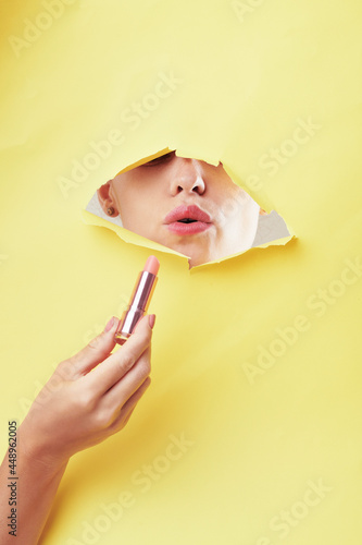 Woman applying lipstick through yellow banner hole and puckering lips