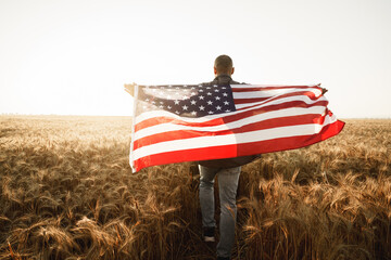 Young man holding American flag on back while standing in wheat field