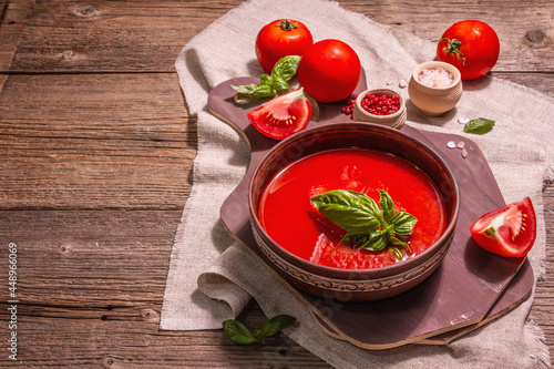 Tomato soup with basil in a bowl. Ripe vegetables, fresh greens, fragrant spices. Vintage wooden table, copy space