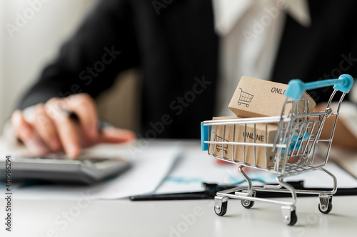 Close up of cart with small box parcel and Businesswoman or accountant working accounting paperwork and business reports on a desk, e-commerce and business online concept.