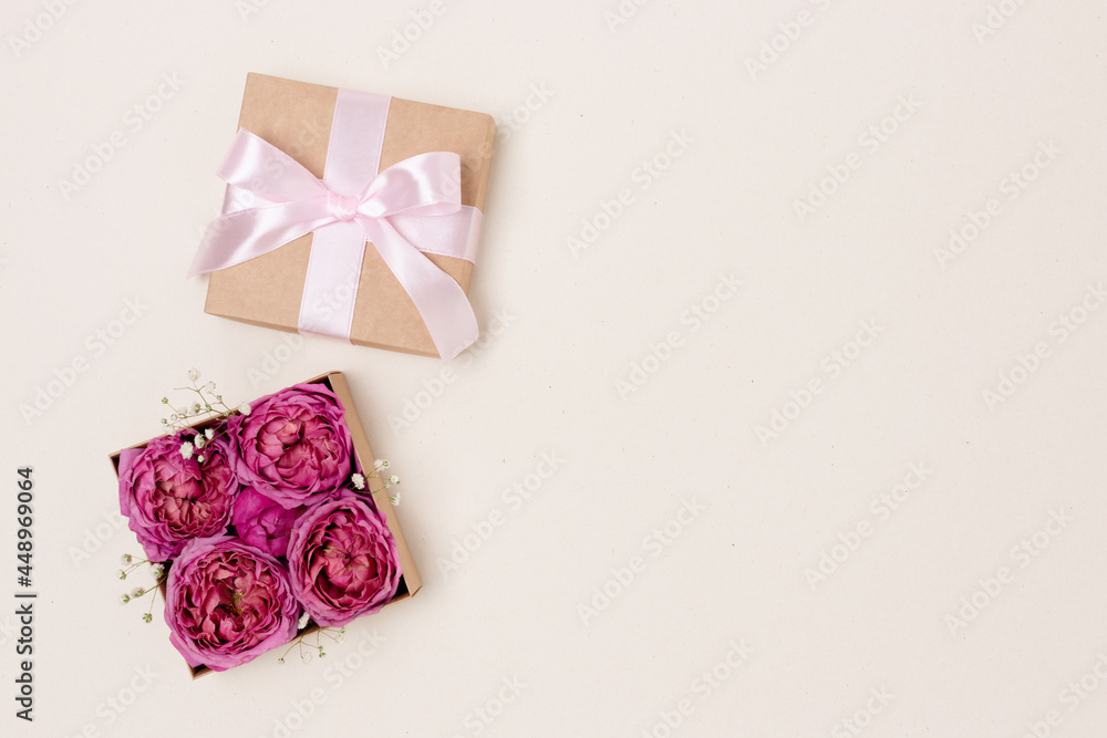 Open gift box with rose flowers inside. Present for springtime holidays on a beige background with copyspace.