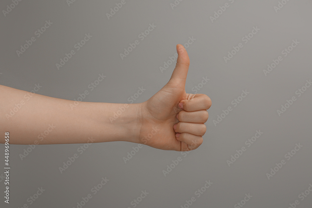 Woman showing thumb up on grey background, closeup