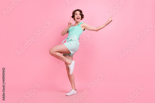 Photo of funny funky young woman dressed turquoise tank-top dancing showing v-signs isolated pink color background
