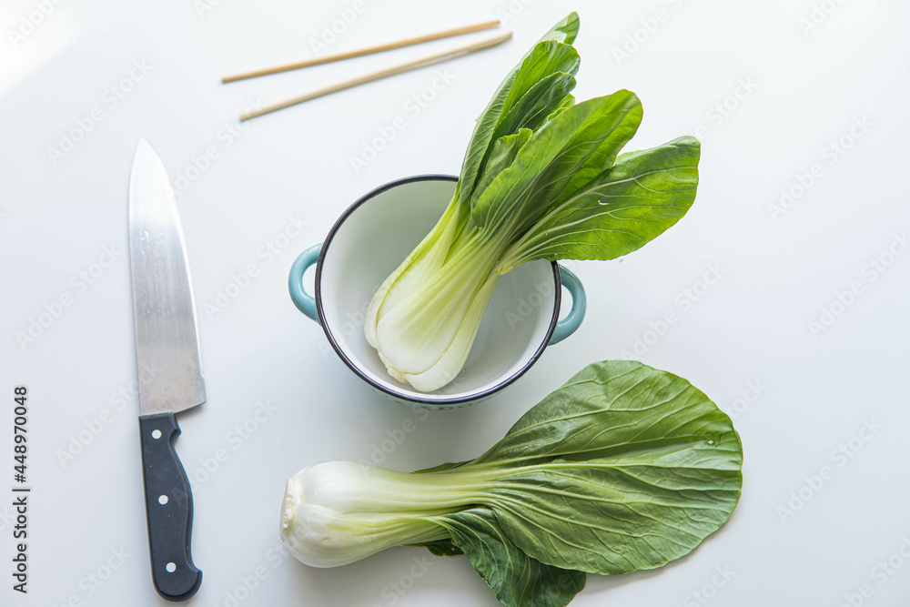 Pak choi or boy choi with a knife next to it and some Chinese sticks over white background
