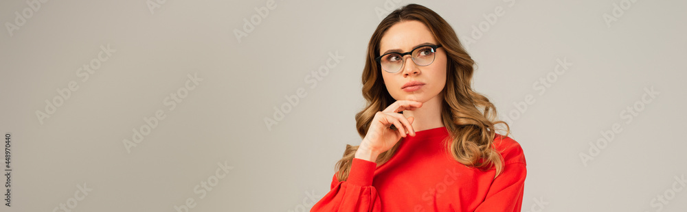 pensive and curly woman in eyeglasses looking away isolated on grey, banner pensive and curly woman in eyeglasses looking away isolated on grey, banner