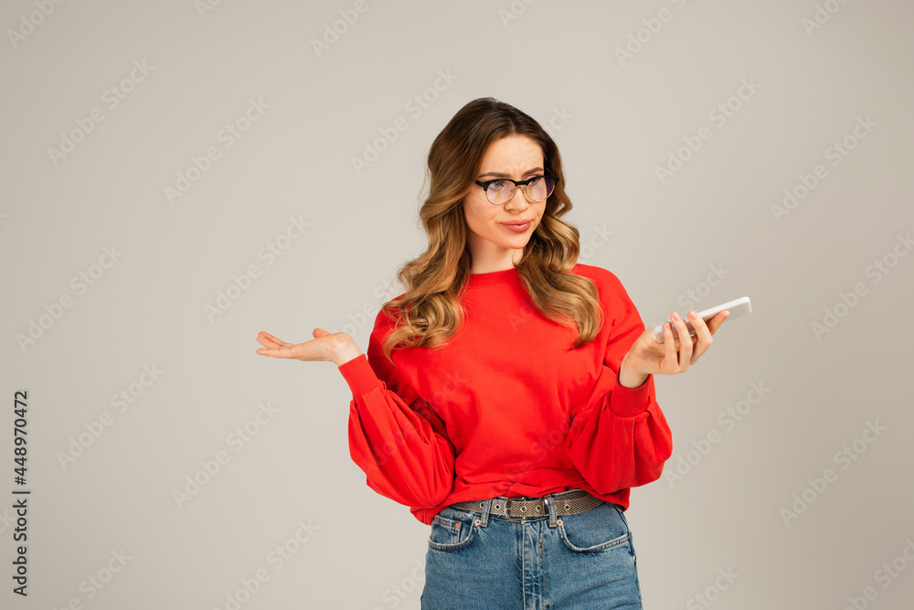 dissatisfied woman in eyeglasses using smartphone isolated on grey dissatisfied woman in eyeglasses using smartphone isolated on grey