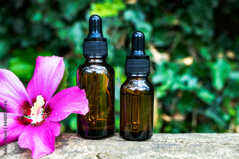 Glass dropper bottles with a pipette and a natural hibiscus flower on a nature background. Organic cosmetics concept. Glass dropper bottles with a pipette and a natural hibiscus flower on a nature background. Organic cosmetics concept.