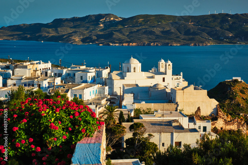 Picturesque scenic view of Greek town Plaka on Milos island over red geranium flowers