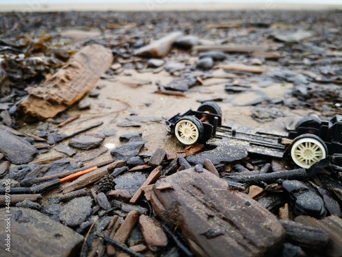 Broken toy car, thrown ashore by the waves of the Baltic Sea with pieces of wood, on a stormy morning 