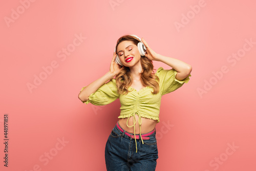 smiling woman adjusting wireless headphones on pink