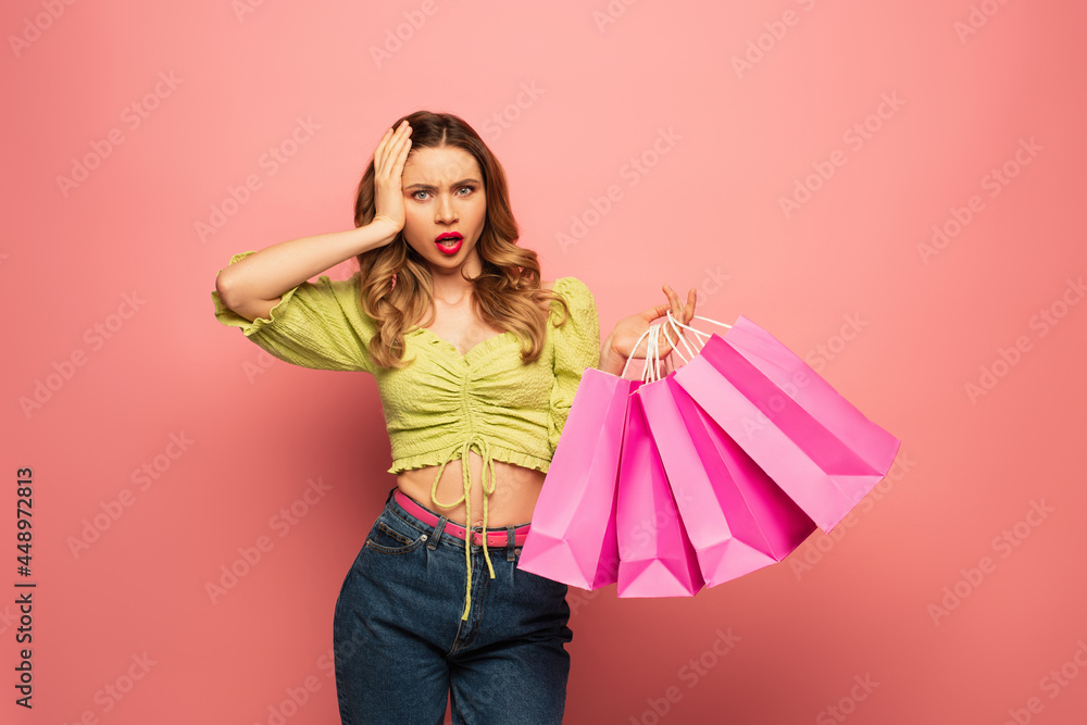 shocked woman holding shopping bags and looking at camera isolated on pink shocked woman holding shopping bags and looking at camera isolated on pink