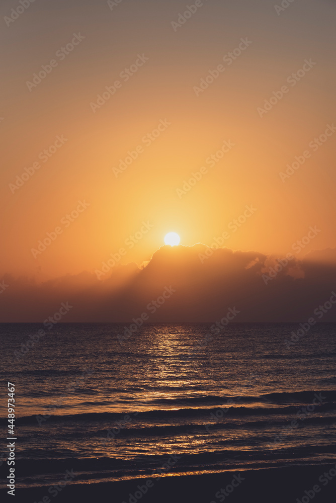 Amanecer en la playa con vistas al Mar Mediterráneo con cielo anaranjado y nublado.