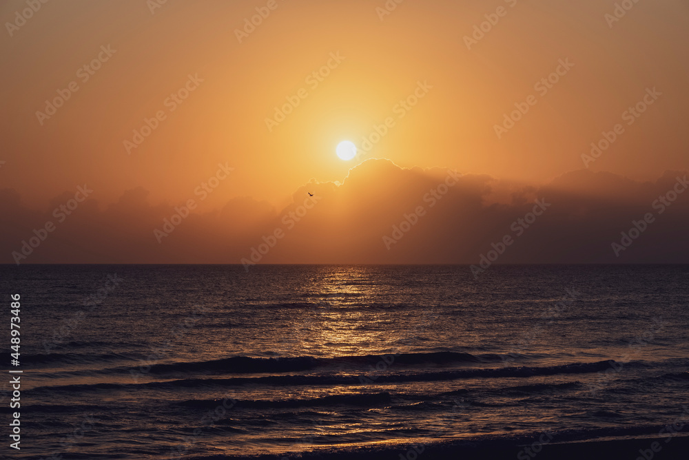 Amanecer en la playa con vistas al Mar Mediterráneo con cielo anaranjado y nublado.