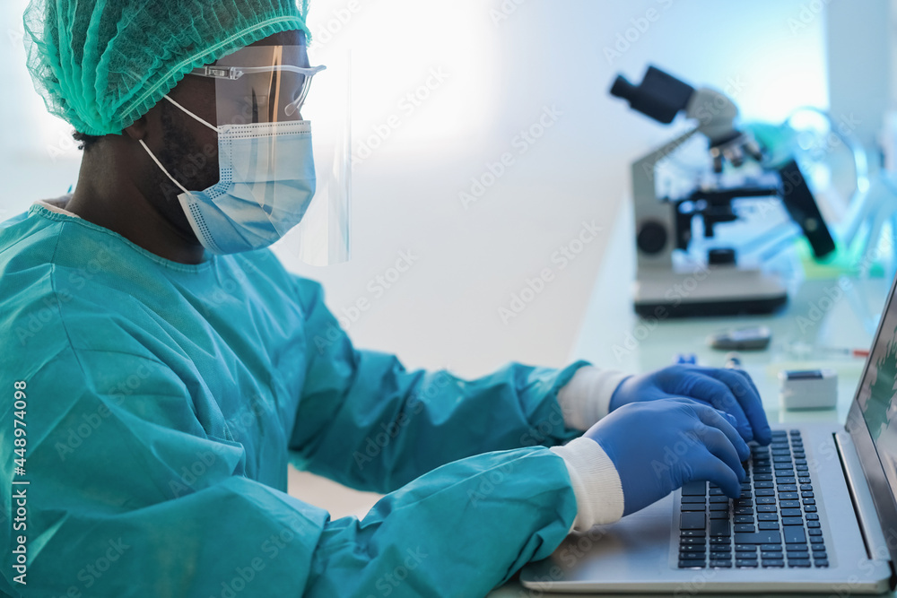 African american doctor man using computer laptop wearing safety mask at work inside hospital - Focus on keyboard African american doctor man using computer laptop wearing safety mask at work inside hospital - Focus on keyboard