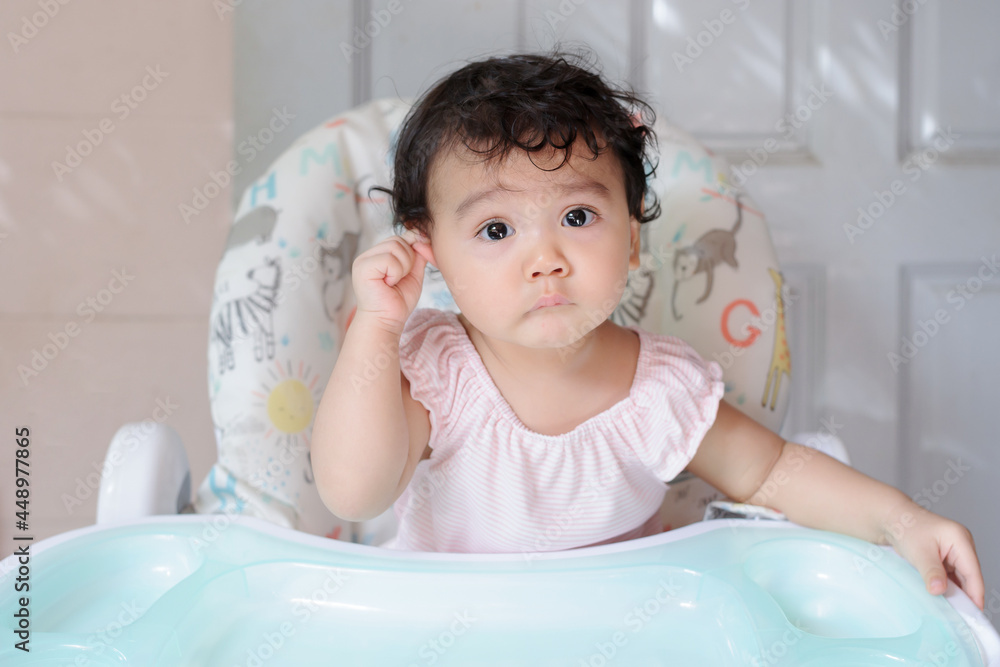 Portrait of a cute little Asian baby girl siting on baby dining table and looking at camera, baby expression concept Portrait of a cute little Asian baby girl siting on baby dining table and looking at camera, baby expression concept