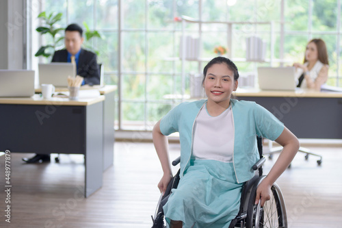 Smiling young Asian woman office worker in wheelchair look at camera, disabled people working with colleague at workplace