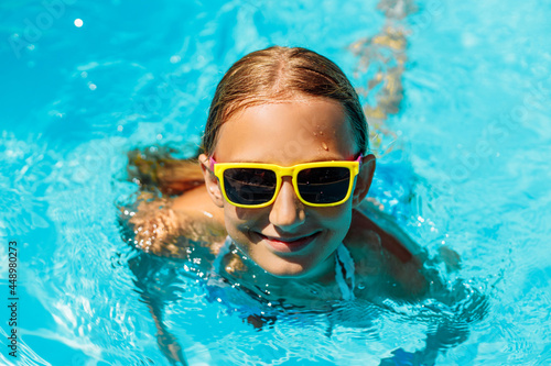 Little girl in sunglasses swimming in the clear blue water of the pool while on vacation in a warm tropical country on a sunny warm summer day