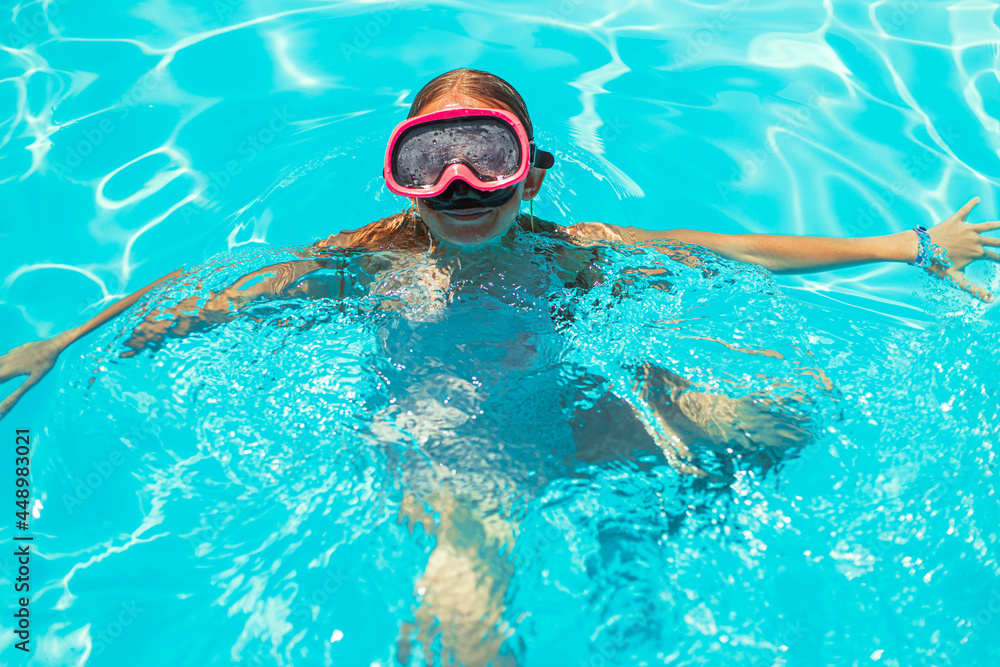 Cute little girl swims in the pool wearing diving goggles, Child smiles and looks at the camera, Happy child plays in the pool