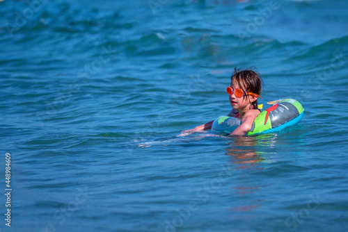 Beautiful young girl swimming in exotic sea and catches the wave. Concept: ocean vacation with kid and family holiday on tropical island. Copy space.