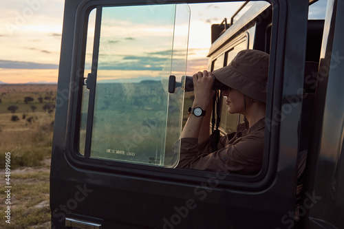 girl standing around a tourist car and looking through binoculars. Against the background of the sunset © monchak