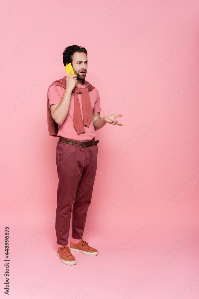 Full length of confused man talking on mobile phone on pink background Full length of confused man talking on mobile phone on pink background