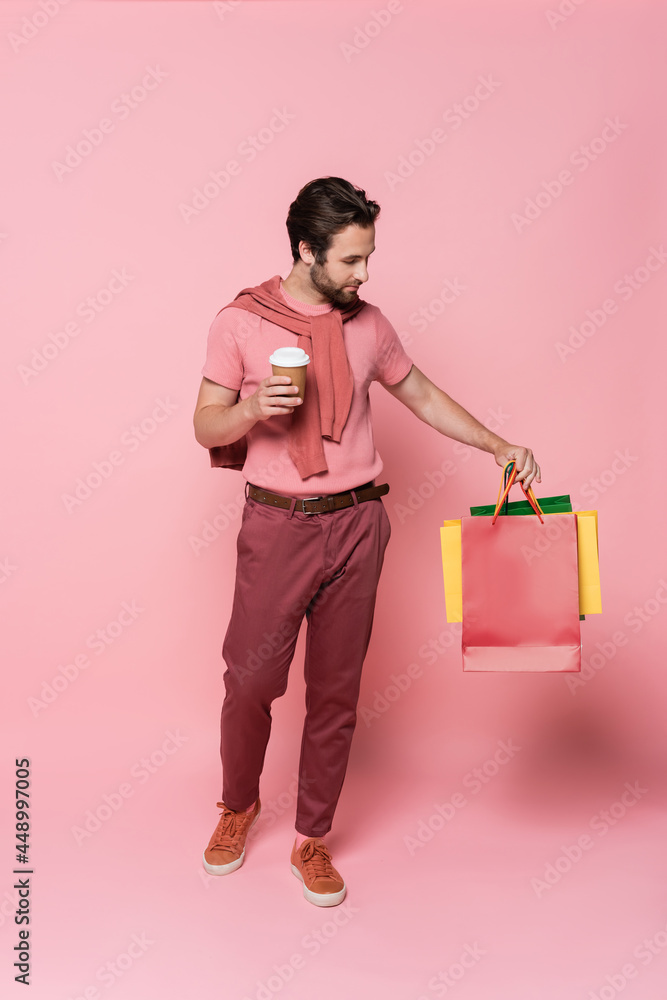 Man with takeaway cup looking at shopping bags on pink background Man with takeaway cup looking at shopping bags on pink background