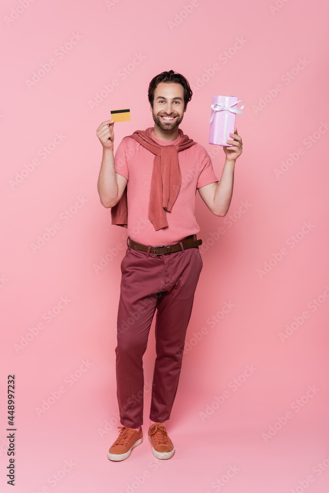 Smiling man with credit card and gift box on pink background Smiling man with credit card and gift box on pink background