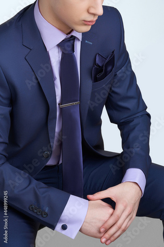 Cropped shot of a man in blue office suit and light violet shirt. Formal wear is completed by blue silk tie, silk handkerchief to match, steel tieclip and cufflinks.  photo