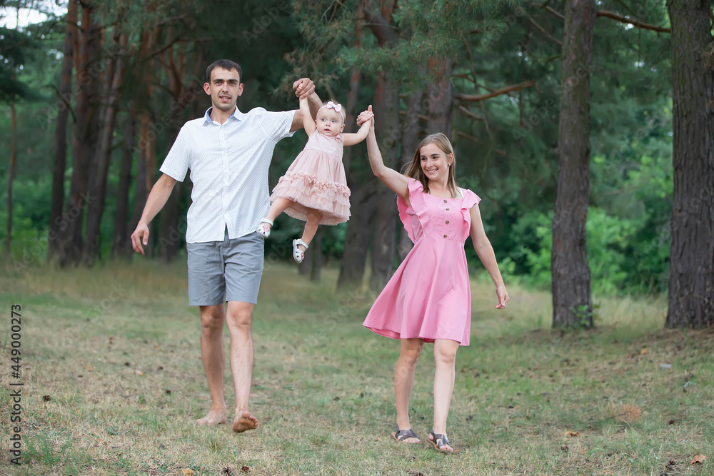 Husband, wife and their little daughter for a walk in the park. Happy dad and mom throws up their little laughing one-year-old daughter. Husband, wife and their little daughter for a walk in the park. Happy dad and mom throws up their little laughing one-year-old daughter.