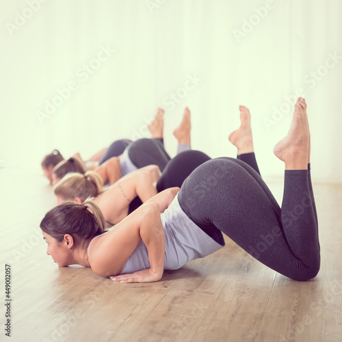 Group of young sporty sexy women in yoga studio, practicing yoga lesson with instructor, forming a line in Shishosana bent puppy dog asana pose. Healthy active lifestyle, working out indoors in gym