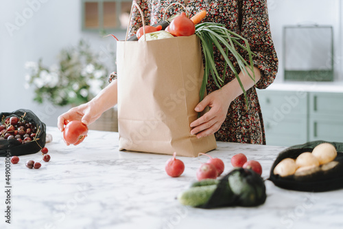 Woman unpacking vegetables from paper grocery bag photo