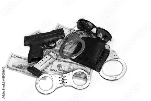 Gun and money. 9 mm pistol gun bullets strewn and dollar banknotes on white. Semi Automatic handgun firearm with mags and rounds, leather wallet in a pile of dollar bills with handcuffs and sunglasses
