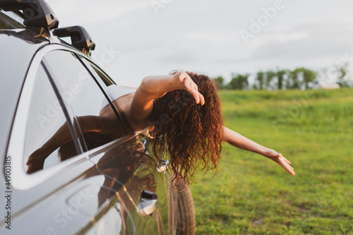 Beautiful young woman travels by car, leaning out the window and having fun photo