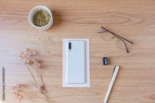 Home office desk mock up with smartphone, accessories, stationary and wild flowers on wooden background. Flat lay, top view. Lady boss concept.
