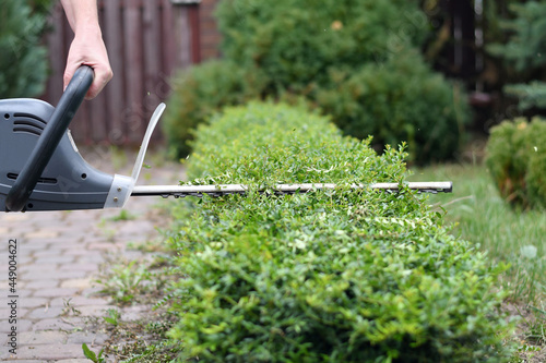 Hands holding electric hedge clippers for trimming green bushes. Selective focus. Low DOF.