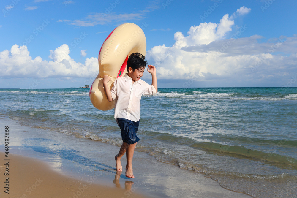 Child wearing colorful inflatable swim ring running on summer beach, kid on tropical sand beach, happy boy spending time and having fun on summer holiday vacation