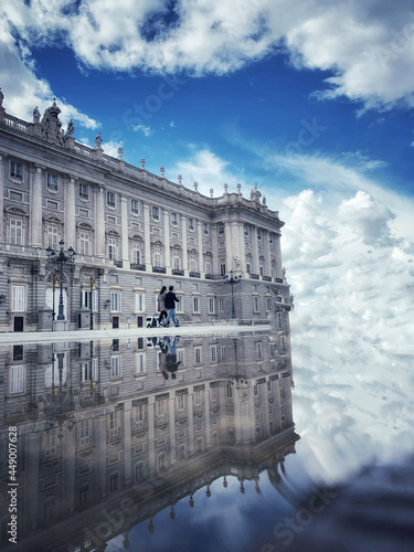 Vertical shot of a couple walking near the Royal Palace of Madrid in Spain near a reflective lake