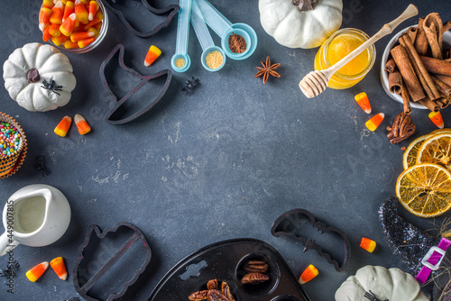Halloween Gingerbread Cookies cooking background. Autumn holiday baking concept, ingredients, spices, halloween symbol cookie cutters - pumpkin, ghost, bat, witch hat, top view black table copy space