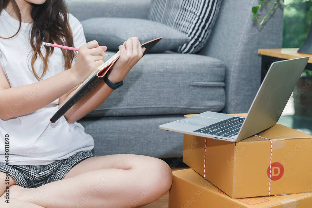 Fototapeta premium Successful entrepreneur business woman with online sales and Parcel shipping in her home office. Woman checking order on notebook.