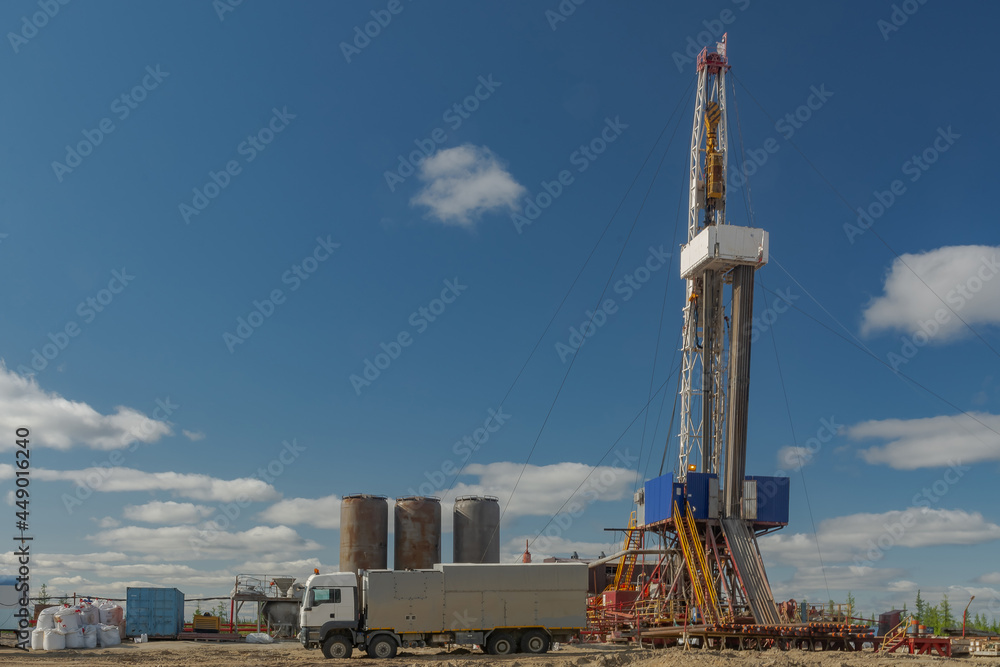 The drilling rig is included in the landscape of the oil and gas field. Infrastructure, communications and drilling equipment are visible. The drilling rig has equipment for well cementing