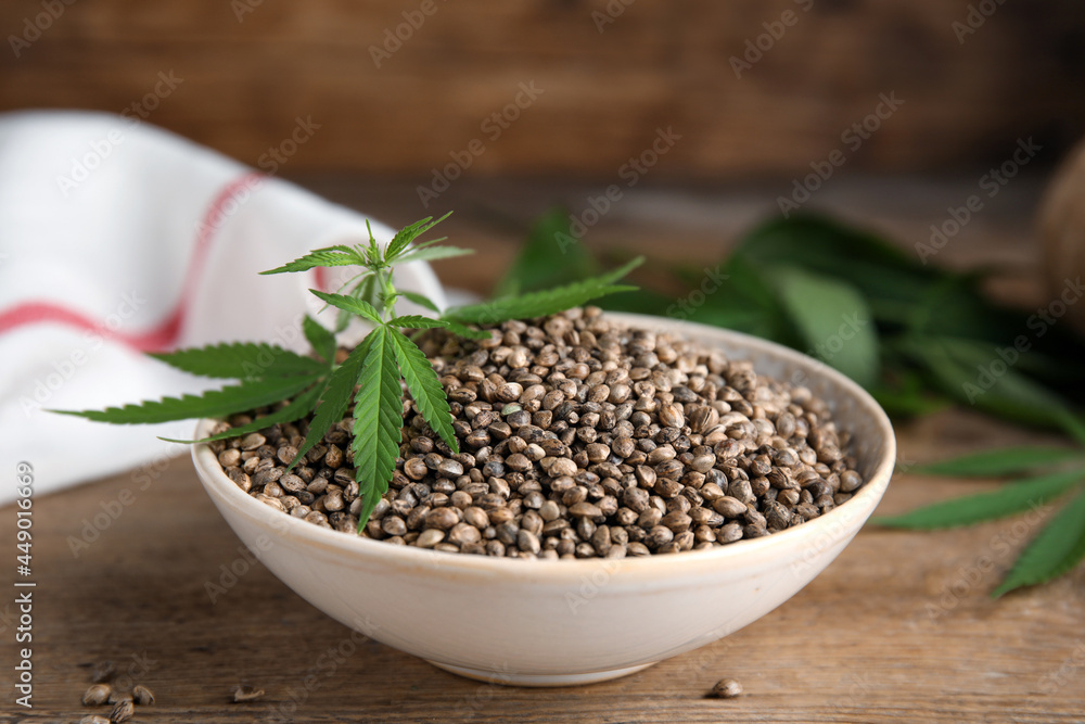 Bowl with hemp seeds and leaves on wooden table Bowl with hemp seeds and leaves on wooden table