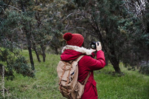 backpacker caucasian woman taking picture with camera in forest during winter or autumn season. Lifestyle and nature