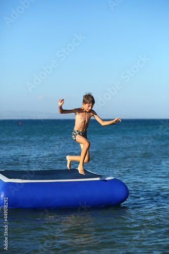 Caucasian boy of nine year old having fun and jumping in to the sea  from the inflatable beach aqua trampoline
